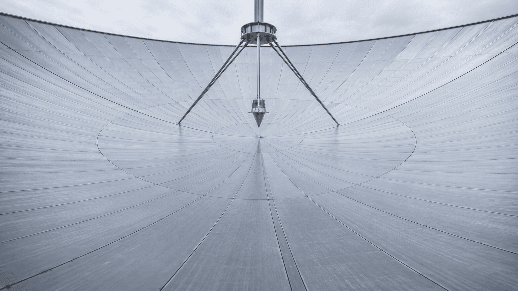Inside a radio telescope dish, radial metal panels converge under a pointed feed held above the center by thin struts